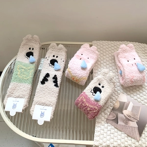 Close-up of soft coral fleece socks with cute 3D cartoon animal designs on a glass table