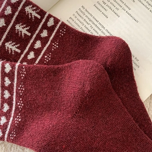 Close-up of red wool socks featuring white jacquard patterns on vintage book props