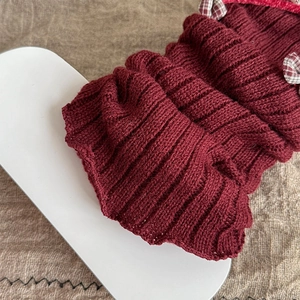 Detail of burgundy ribbed knit leg warmers with black and white plaid bow accents
