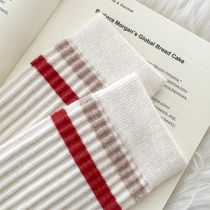 Detail of ribbed knit texture on cream socks with red and khaki stripes on a plush rug