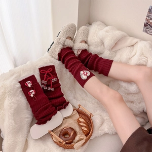 Detail of red knit leg warmers with white heart embroidery and ribbon bows on plush rug