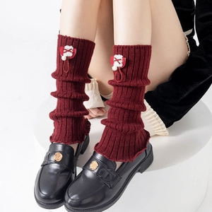 Red knit leg warmers with bows paired with black rose-buckle loafers on a white platform