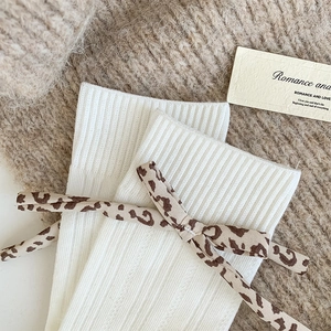 Close-up of off-white ribbed knit socks with leopard print bow on soft knit background
