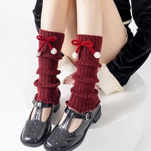 Detail of burgundy knitted leg warmers featuring red velvet bows and white plush balls