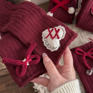 Detail of burgundy knit leg warmers with white lace heart and red ribbon bow accent