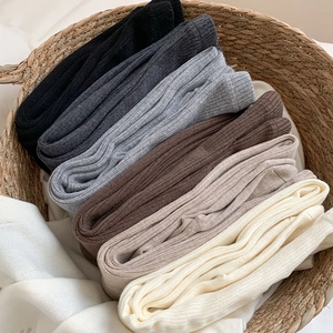 Detailed view of ribbed wool leggings in various neutral colors inside a basket