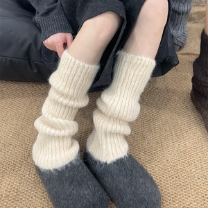 Cream knit leg warmers paired with grey slippers on a textured rug for winter