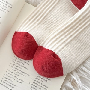 Close-up of cream white ribbed socks with red toe detail on a plush white background