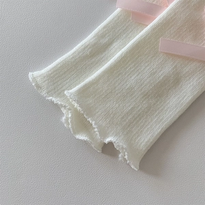 Detailed view of cream knit leg warmers with pink silk bows and scalloped ruffle edges