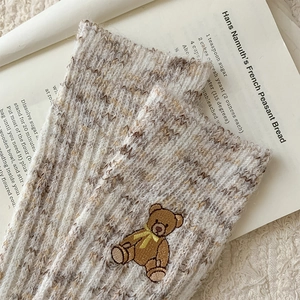 Detailed close-up of thick knitted melange socks with cute bear embroidery on soft fabric