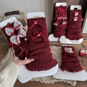 Detail of red cable knit leg warmers with lace bows, plaid ribbons and white pom-poms