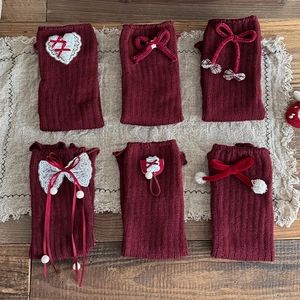 Detail of red knit leg warmers with lace hearts, velvet bows, and fuzzy white pom-poms