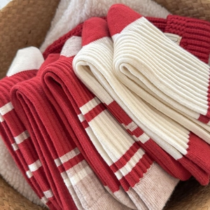 Close-up of red and striped knit mid-calf socks neatly stacked in a warm wool basket