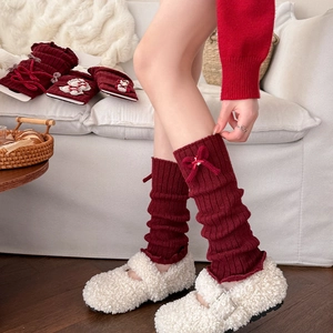 Close-up of wine red knitted leg warmers with ribbon bow and ribbed texture detail