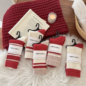 Detail of five pairs of striped crew socks in warm autumn colors on a soft white fur rug