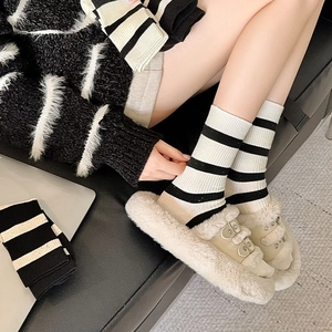 Detail of black and white striped crew socks paired with beige plush metal buckle slippers