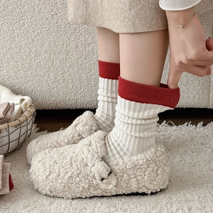 Close-up of white ribbed socks with red trim paired with fleece-lined winter slippers