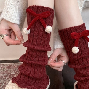 Detail of red cable knit leg warmers featuring velvet bows and white faux fur pom-poms