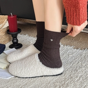 Close-up of brown ribbed socks featuring a delicate golden horse charm and white plush slippers