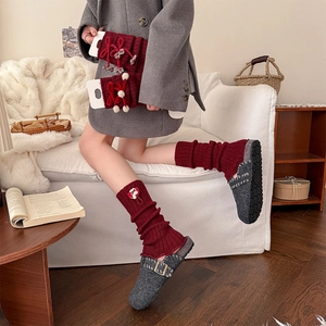 Detail of red knitted leg warmers with bows, fur balls and ruffle edges in home setting