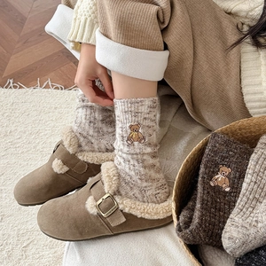 Close-up of cute bear embroidery on beige knit socks with warm brown mule slippers
