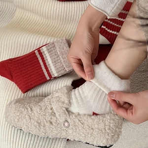 Close-up of red and white striped winter knit socks worn with off-white fuzzy mules