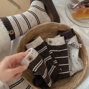 Detail of wool socks with bow, wooden button and vintage stripes in cozy basket