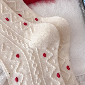 Detailed knit texture of creamy wool socks featuring elegant red polka dot embroidery