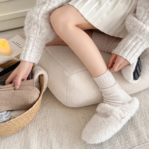 Detailed texture of white ribbed wool socks and plush slippers in a cozy home setting