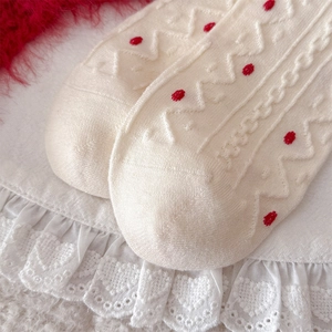 Detail of cream knit sock featuring red polka dots and intricate cable knit patterns