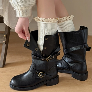 Detail of cream lace trim knitted leg warmers styled with black buckled leather boots