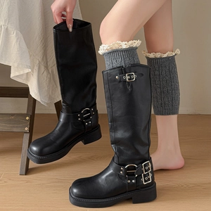 Close-up of black leather motor boots with metal buckles and grey lace knitted leg warmers