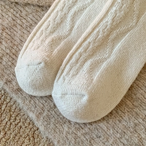 Macro shot of off-white wool socks featuring classic cable knit texture and soft fabric