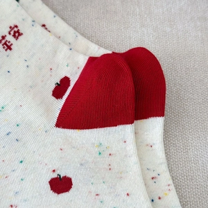 Détail de chaussettes en maille crème avec motif de pomme rouge et broderie de chance
