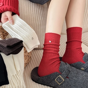 Detail of red festive wool socks featuring ribbed texture and metal horse charm accessory
