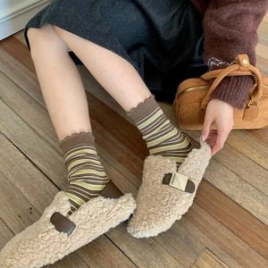 Close-up of beige fleece mule shoes with brown leather straps and gold metal buckles