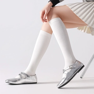 Solid white knit knee-high socks paired with silver Mary Janes and a pleated skirt