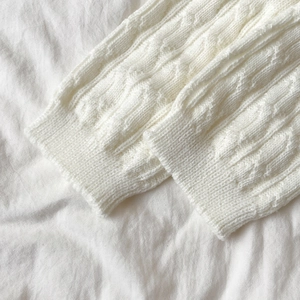 Close-up of white cable knit leg warmers with lace trim showing soft texture and details