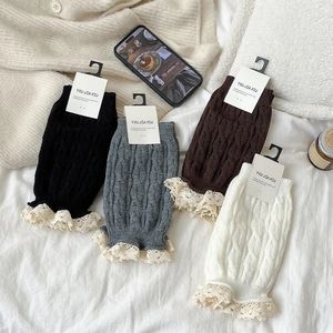 Close-up of cable knit leg warmers with delicate lace trim in various soft colors