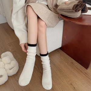 Detailed close-up of warm off-white knit socks with black trim on a model in home setting