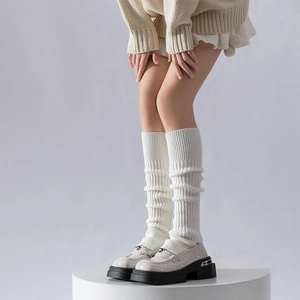 White vertical knit leg warmers paired with black chunky loafers on a white stand