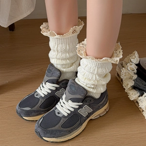Close-up of cream knit leg warmers with delicate lace trim edges and ribbed texture
