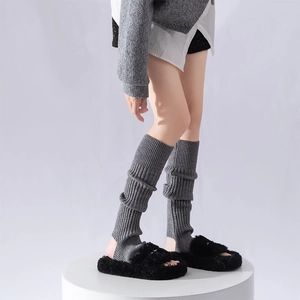 Detailed texture of dark grey ribbed knit leg warmers paired with black fuzzy slippers