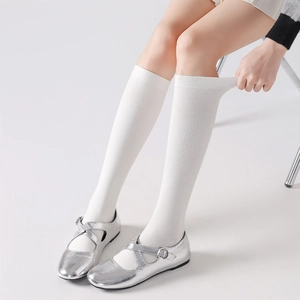 Close-up of white ribbed knee-high socks with silver metallic Mary Jane shoes and cross straps