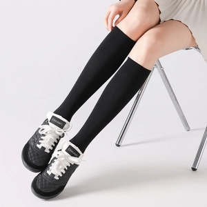 Detailed knit texture of black knee-high socks paired with a white pleated skirt and sneakers