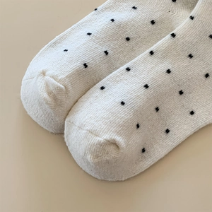 Close-up of white wool blend socks featuring a delicate black heart pattern and knit texture