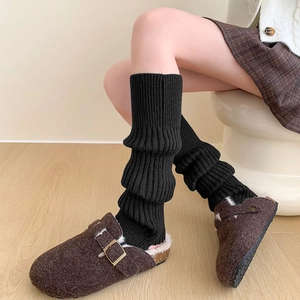 Gros plan sur des jambières en tricot noir avec des sandales à boucle sur parquet bois