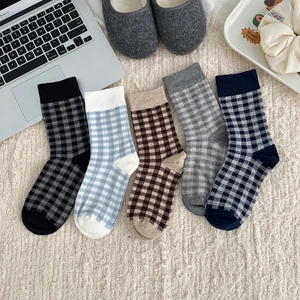 Flat lay of five pairs of plaid crew socks in diverse colors on a cozy home rug