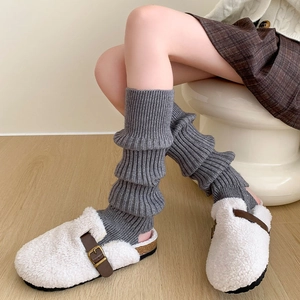 Jambières en tricot gris avec mules en peluche blanches sur parquet clair
