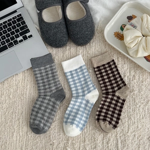 Three pairs of plaid cotton mid-calf socks displayed in a cozy home setting with carpet